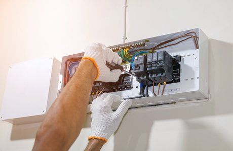 An electrician's gloved hands wiring a distribution board